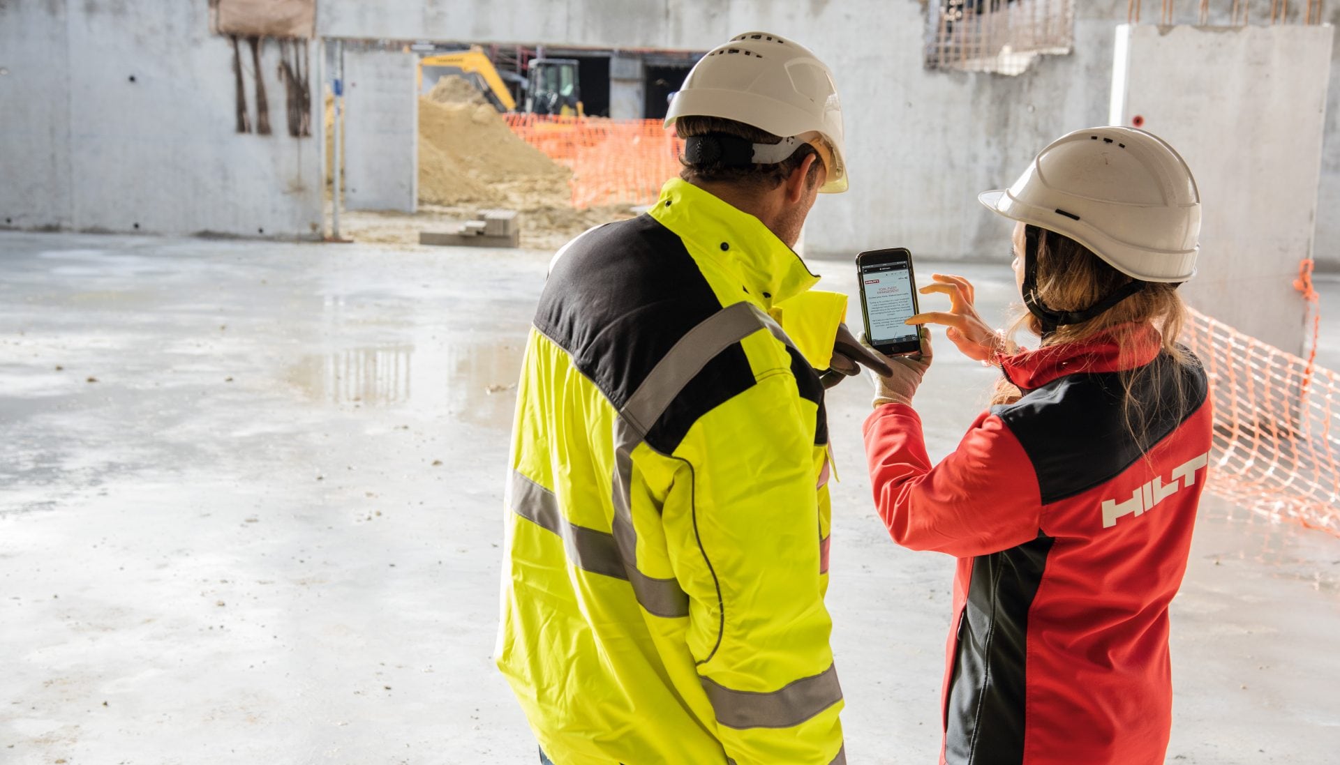 Dvaja pracovníci na stavbe spolu pozerajú do mobilu