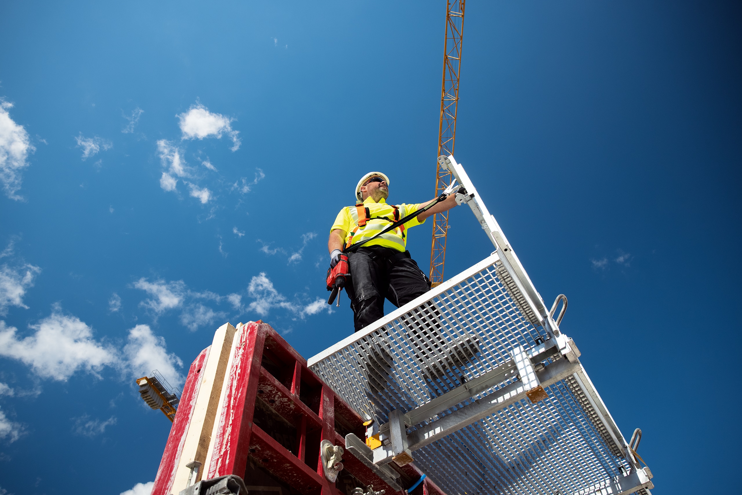 Pracovník stojí na plošine so strojom pripevneným bezpečnostným popruhom