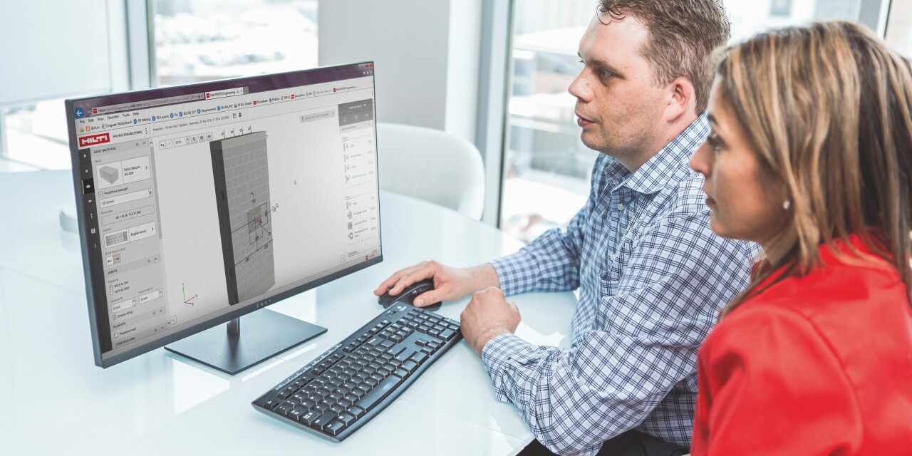 2 people at a desk in front of a desktop screen displaying an anchor design